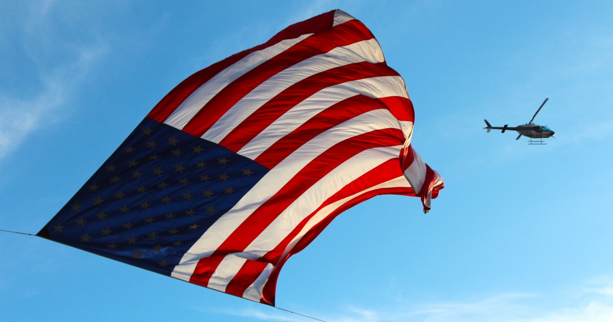 Large US flag and helicopter flying by in background